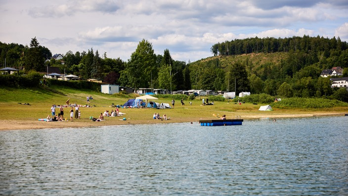 Ein Badesee in NRW, am Ufer sind Zelte und Wohnwägen.