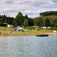 Ein Badesee in NRW, am Ufer sind Zelte und Wohnwägen.