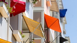 Sonnenschirmen und Markisen, die an einem Mehrfamilienhaus Balkone abschirmen.