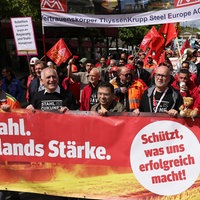 Gruppe von Demonstrierenden mit roten Fahnen und Bannern, vorne rotes Banner mit weißer Aufschrift 'Unser Stahl. Deutschlands Stärke.' und 'Schützt, was uns erfolgreich macht!'