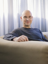 Thomas Riedel, Gründer und Inhaber von Riedel Communications sitzt in einem Sessel und lächelt in die Kamera