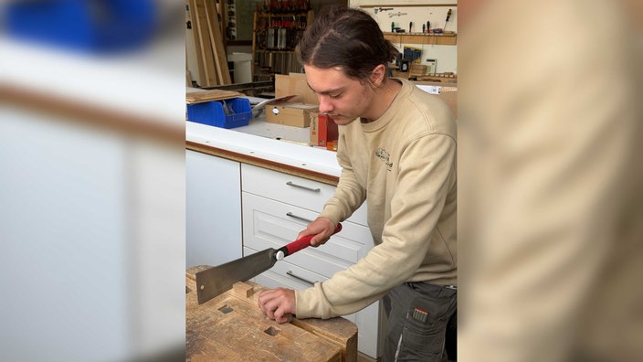 Ein Praktikant bei der Tischlerei Hillebran schneidet ein Stück Holz