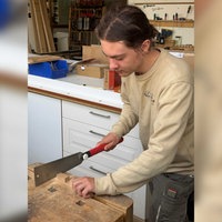Ein Praktikant bei der Tischlerei Hillebran schneidet ein Stück Holz