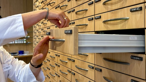 Eine offene Schublade eines Apothekerschrankes, in die jemand greift.
