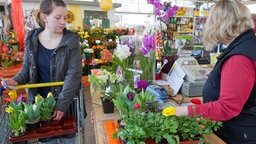Eine Frau bezahlt an der Kasse eines Gartencenters ihre Blumen.