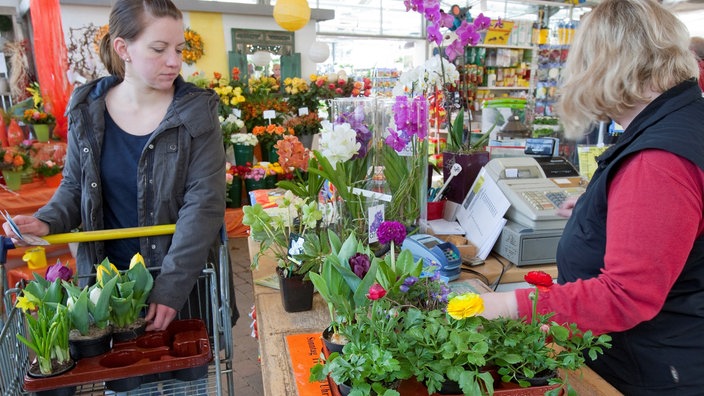 Eine Frau bezahlt an der Kasse eines Gartencenters ihre Blumen.