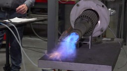Ein längliches Gerät, aus dem blaue Flammen strömen.