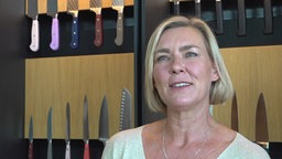 Eine Frau steht vor einer Wand mit Küchenmessern