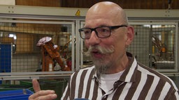 Mann mit Brille steht vor einem Roboter in einer Produktionshalle
