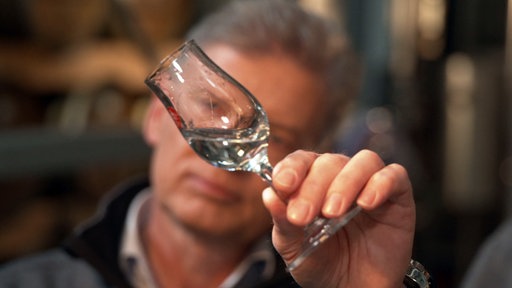 Ein Mann Hält ein Schnapsglas vor sein Gesicht und betrachtet die Flüssigkeit