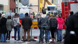 Anwohner und Schaulustige gucken hinter einer Absperrung zu einem explodierten Wohnhaus