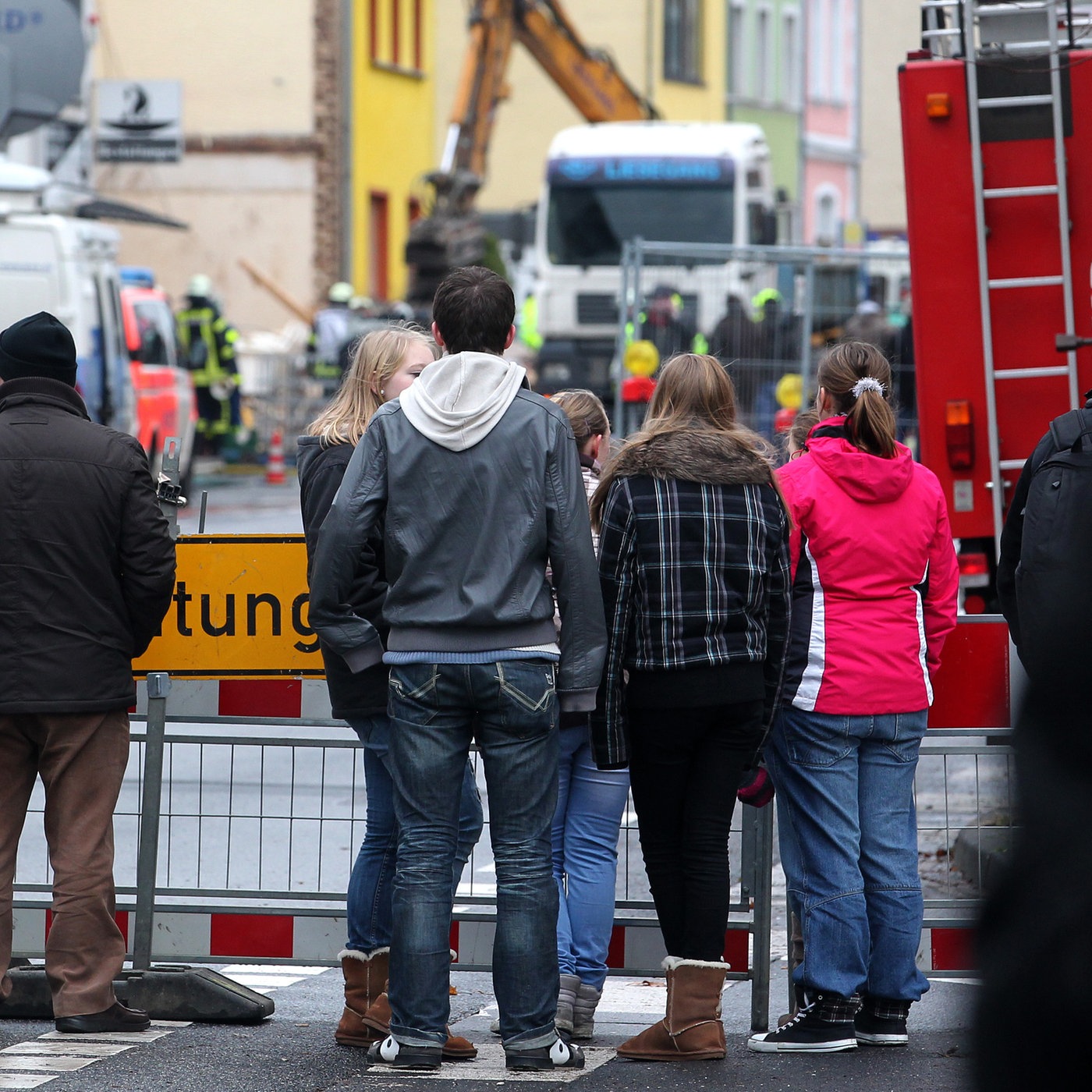 Anwohner und Schaulustige gucken hinter einer Absperrung zu einem explodierten Wohnhaus